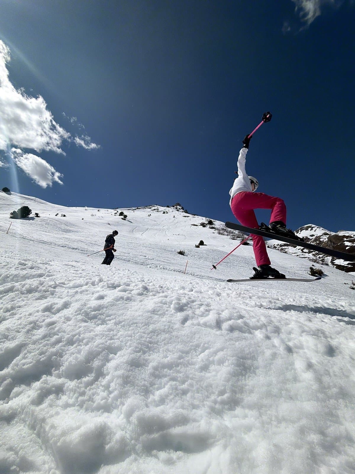 Skier descending a slope with sun flare and Alpine peaks behind